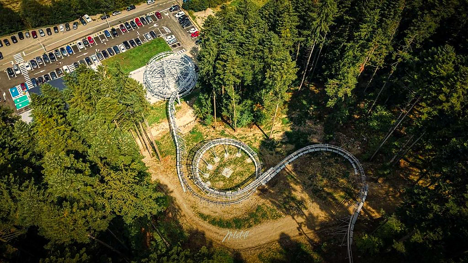 Traseul Forest Coaster văzut din aer: bucla, parcarea și pădurea din jur