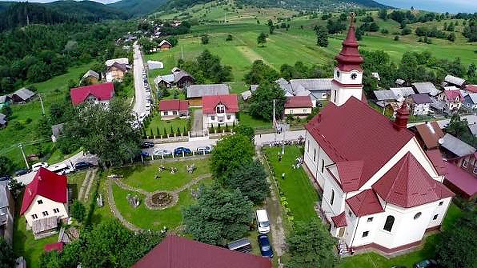 Priveliște de sus asupra satului, cu biserica la mijloc, între câmpuri și dealuri